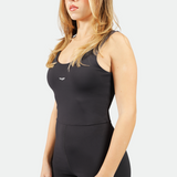 a fit woman wearing  jump suit black with logo white ,plus the background is light grey 