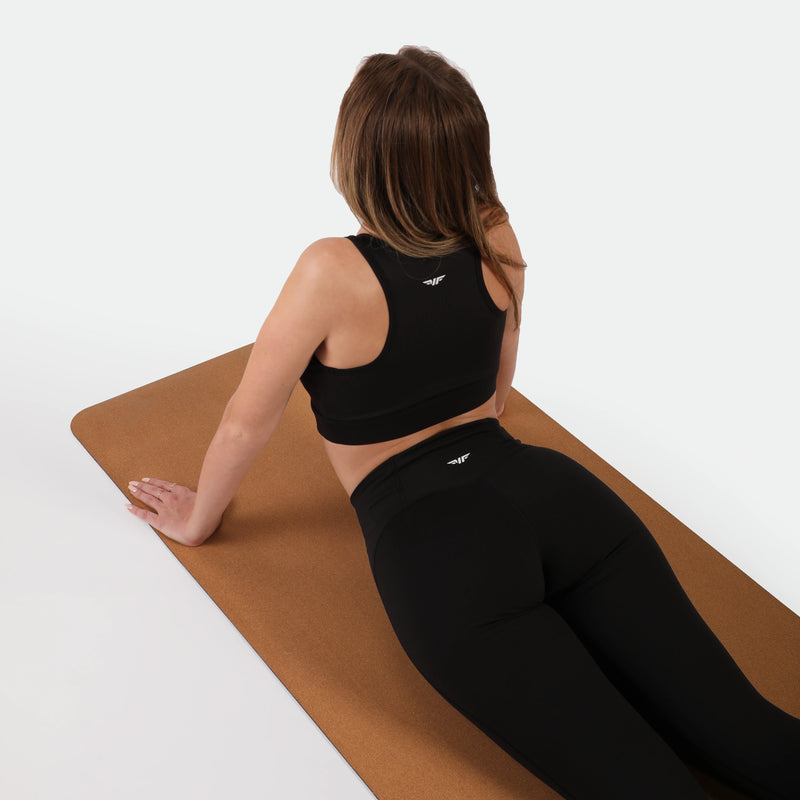 Woman in black athletic wear on a brown mat against a white background