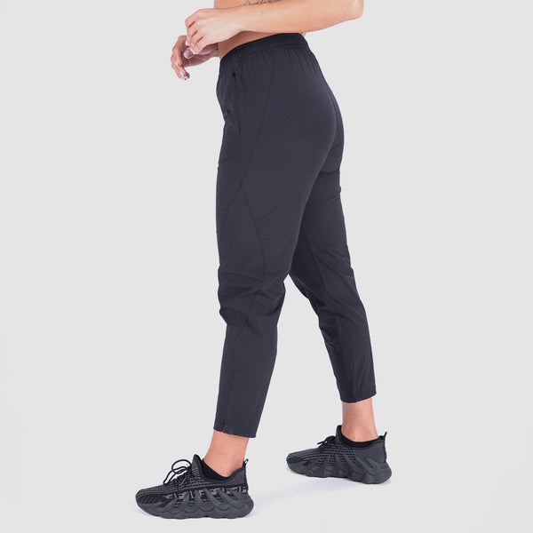 a woman stand at right  and wearing pants black with shoes black ,plus the background is light grey
