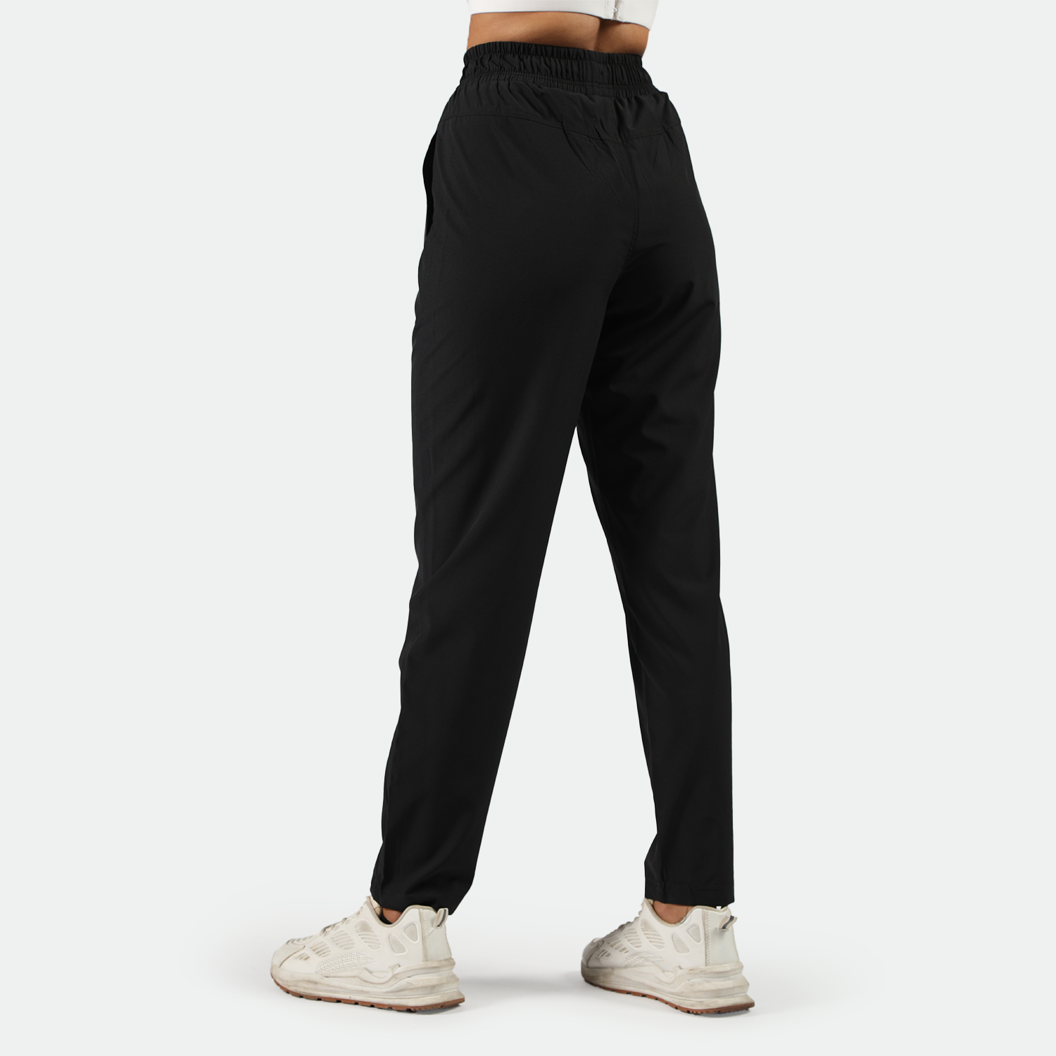 a back view for fit woman wearing black pants with  shoes white ,plus the background is light grey 