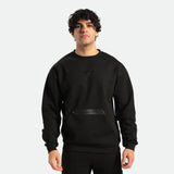A man wearing a black long-sleeved sweatshirt with a kangaroo pocket, standing against a white background.