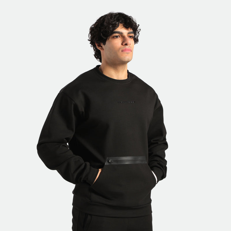 a fit man look at right and here hand inside in pocket kangaroo ,he wearing matching set black , sweatshirt and pants 