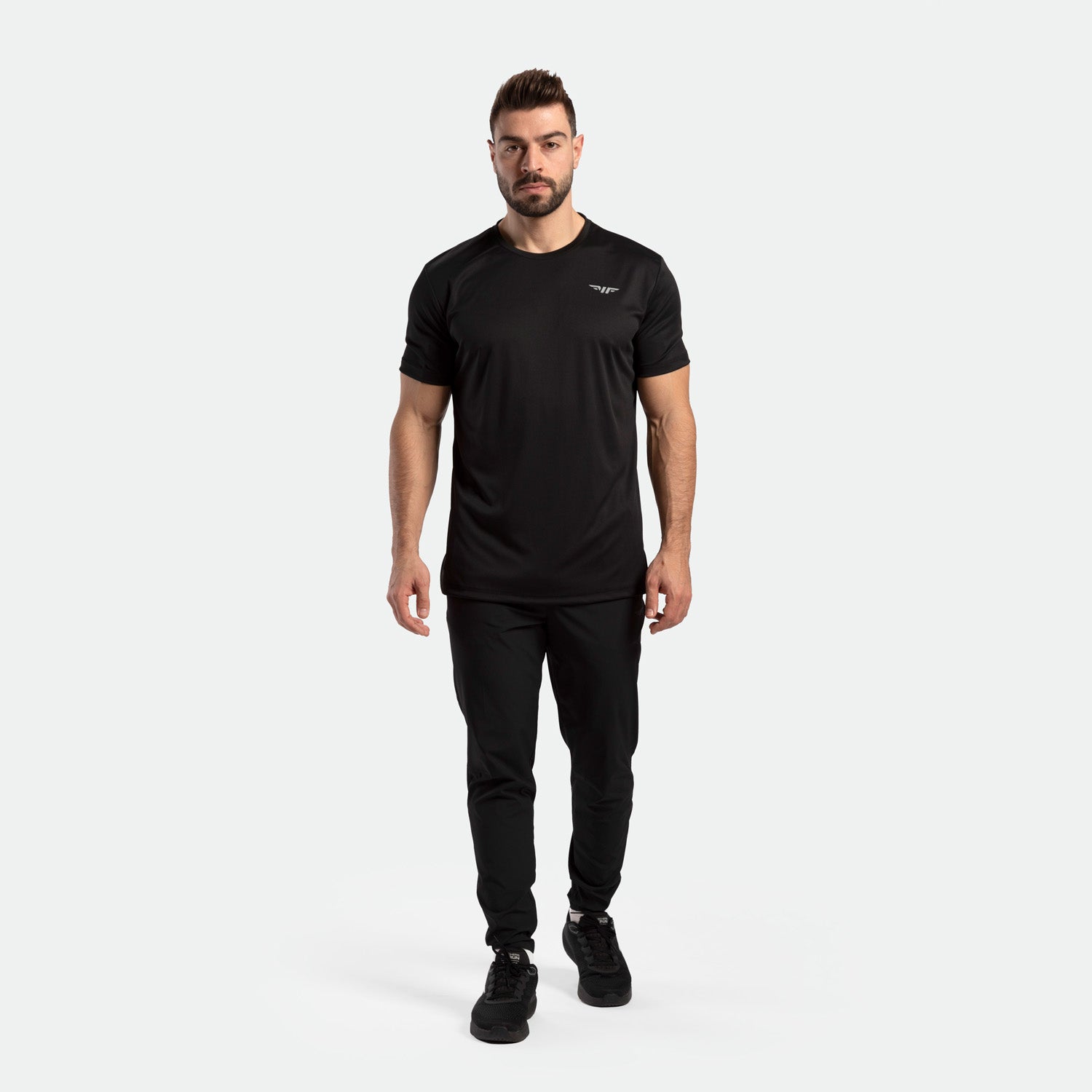 a fit man wearing matching color black  t-shirt with logo and pants and shoes 
