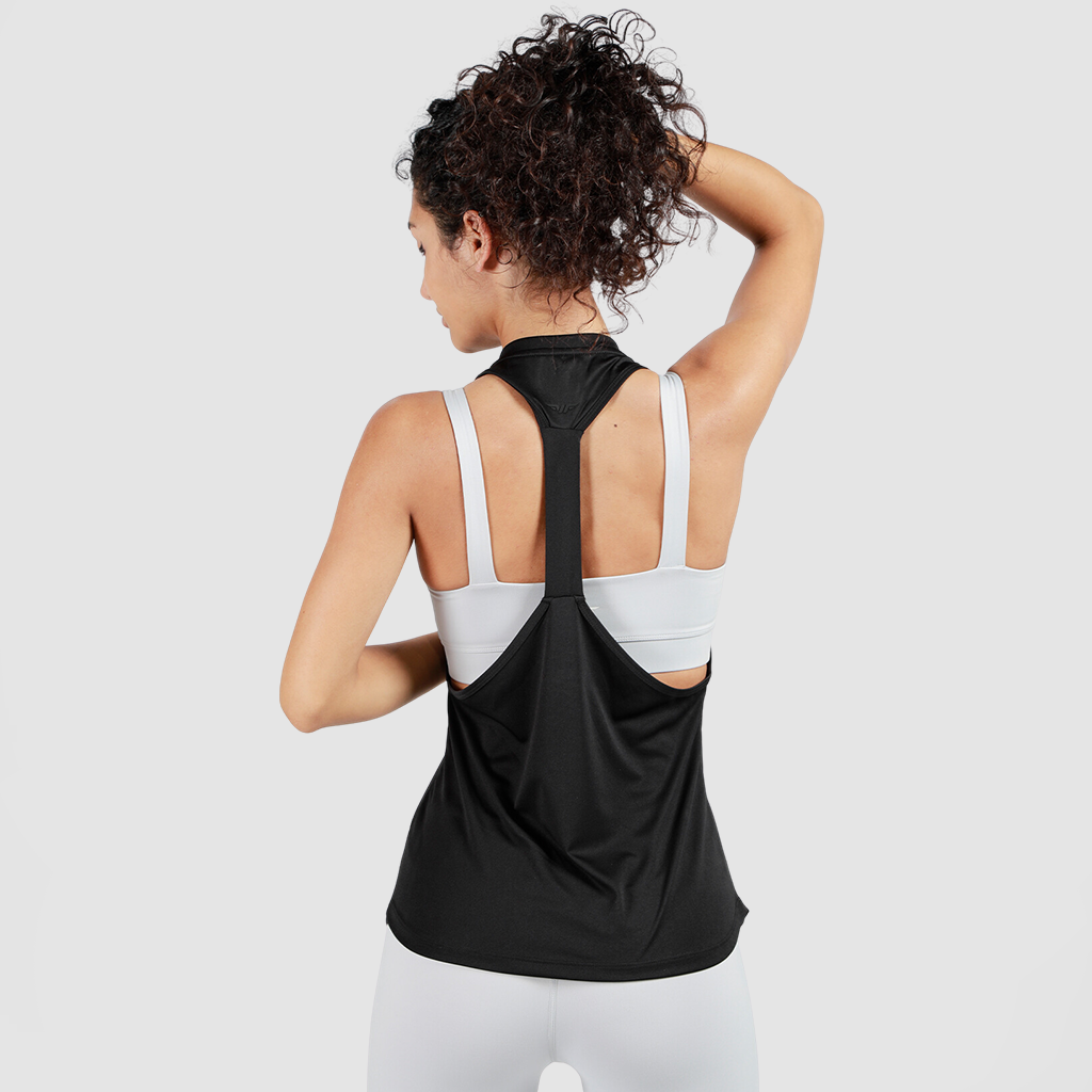 A woman with curly hair in a high ponytail is seen from the back, wearing a black tank top over a white sports bra and leggings, against a plain background.