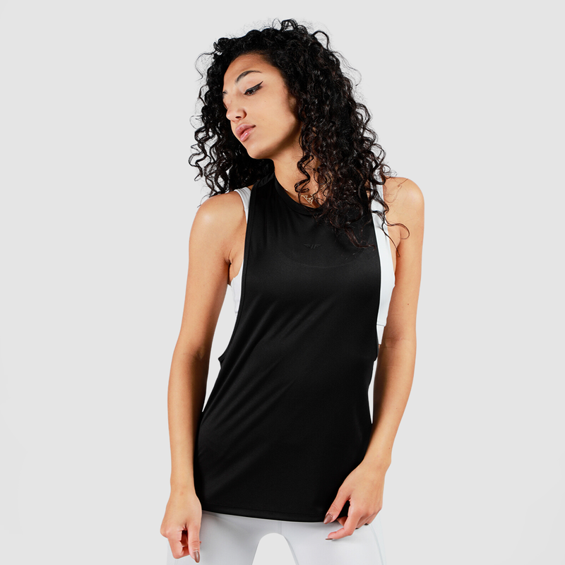 A woman with curly hair poses confidently in a sleeveless black top and white leggings against a plain background, conveying a sporty and stylish vibe.