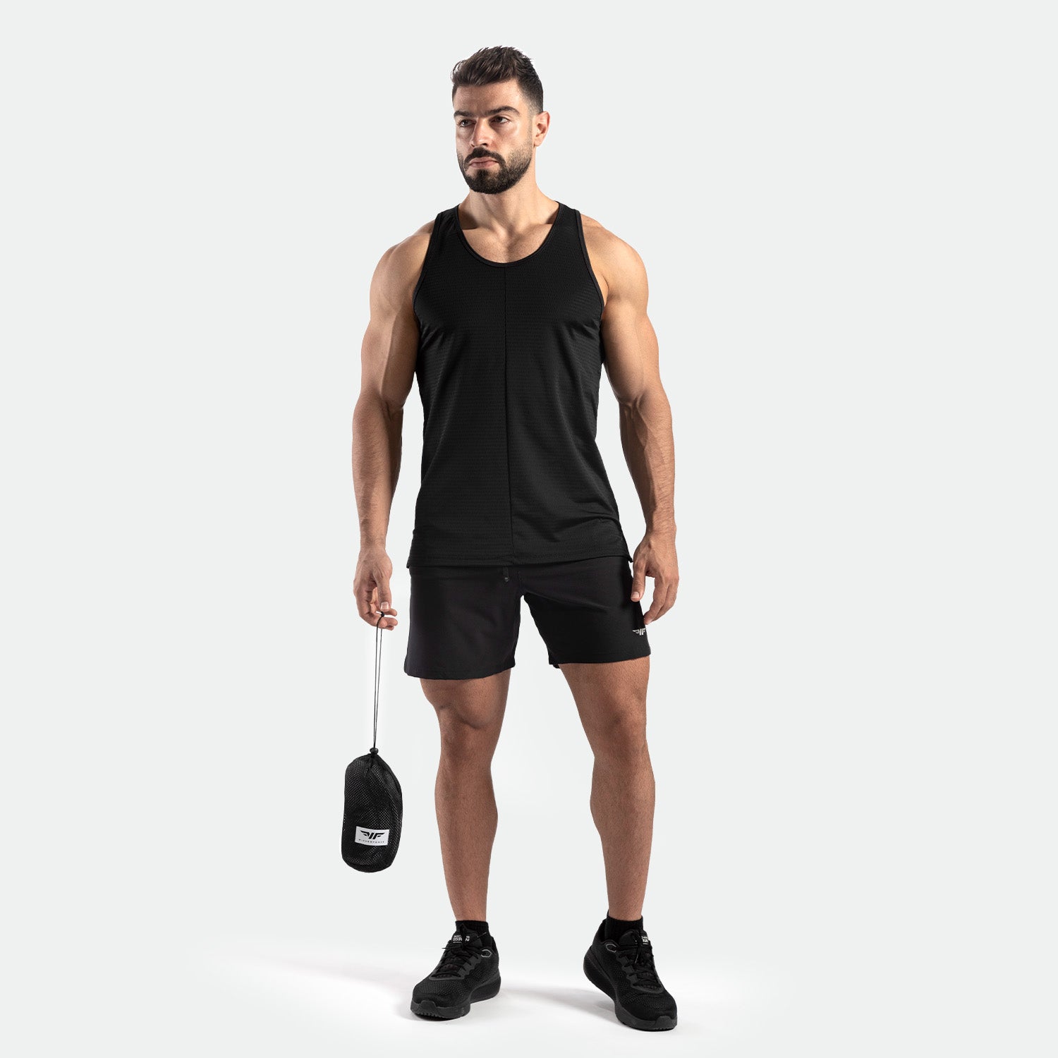 a fit man stand at right and wearing tank black with short black ,plus shoes 