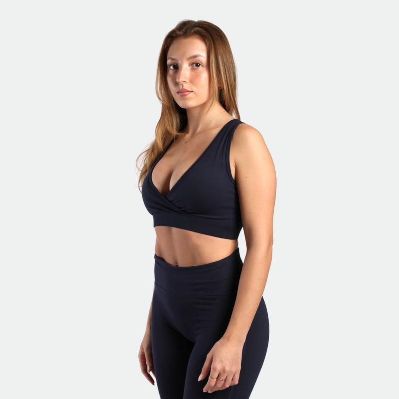 a fit woman stand at right and wearing matching set navy blue ,bra and flared  legging 