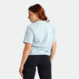 Woman wearing a light blue scrub top and black pants on a white background