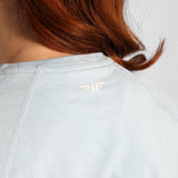 Light gray shirt with a logo on the chest, worn by a person with red hair.