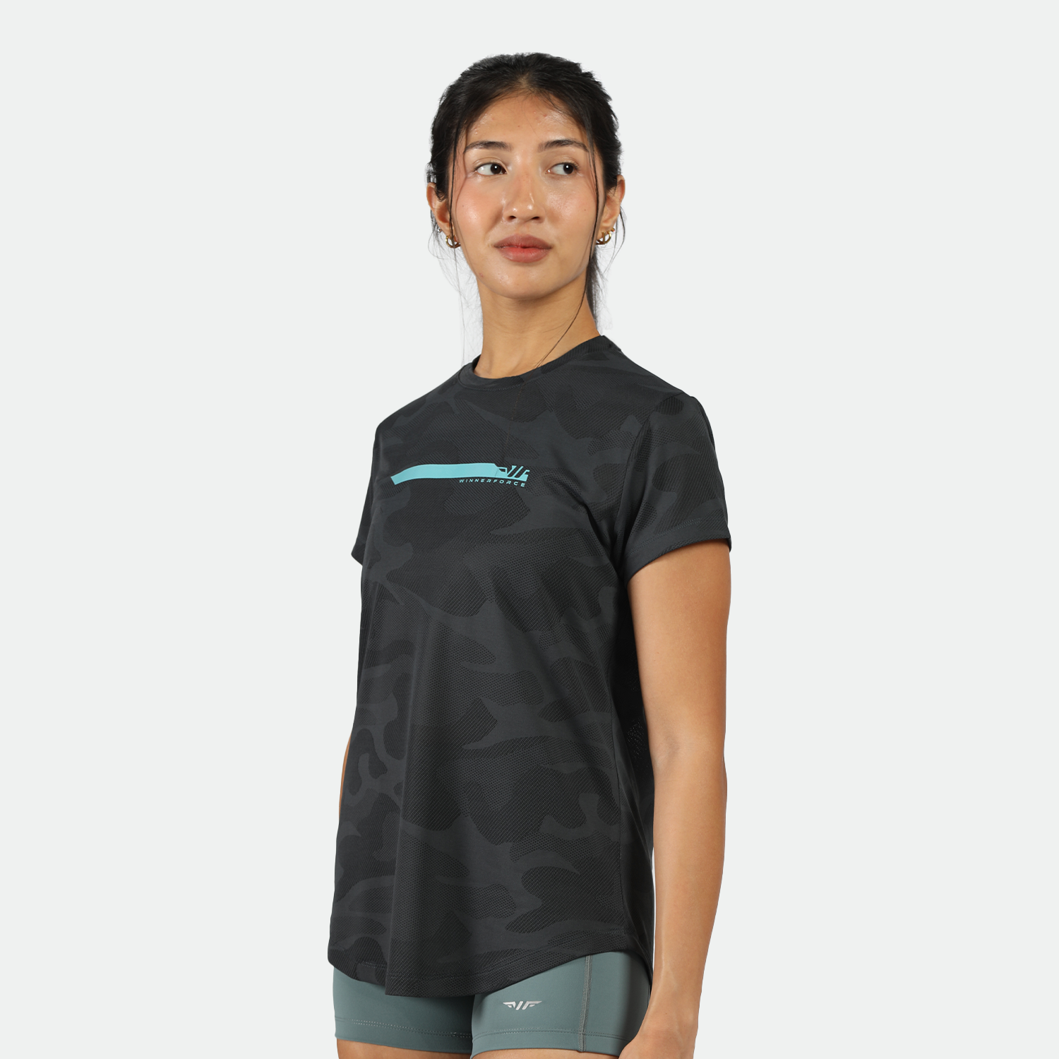 a fit woman stand at right and look at right ,she wearing  t-shirt black with logo ,and short green 
