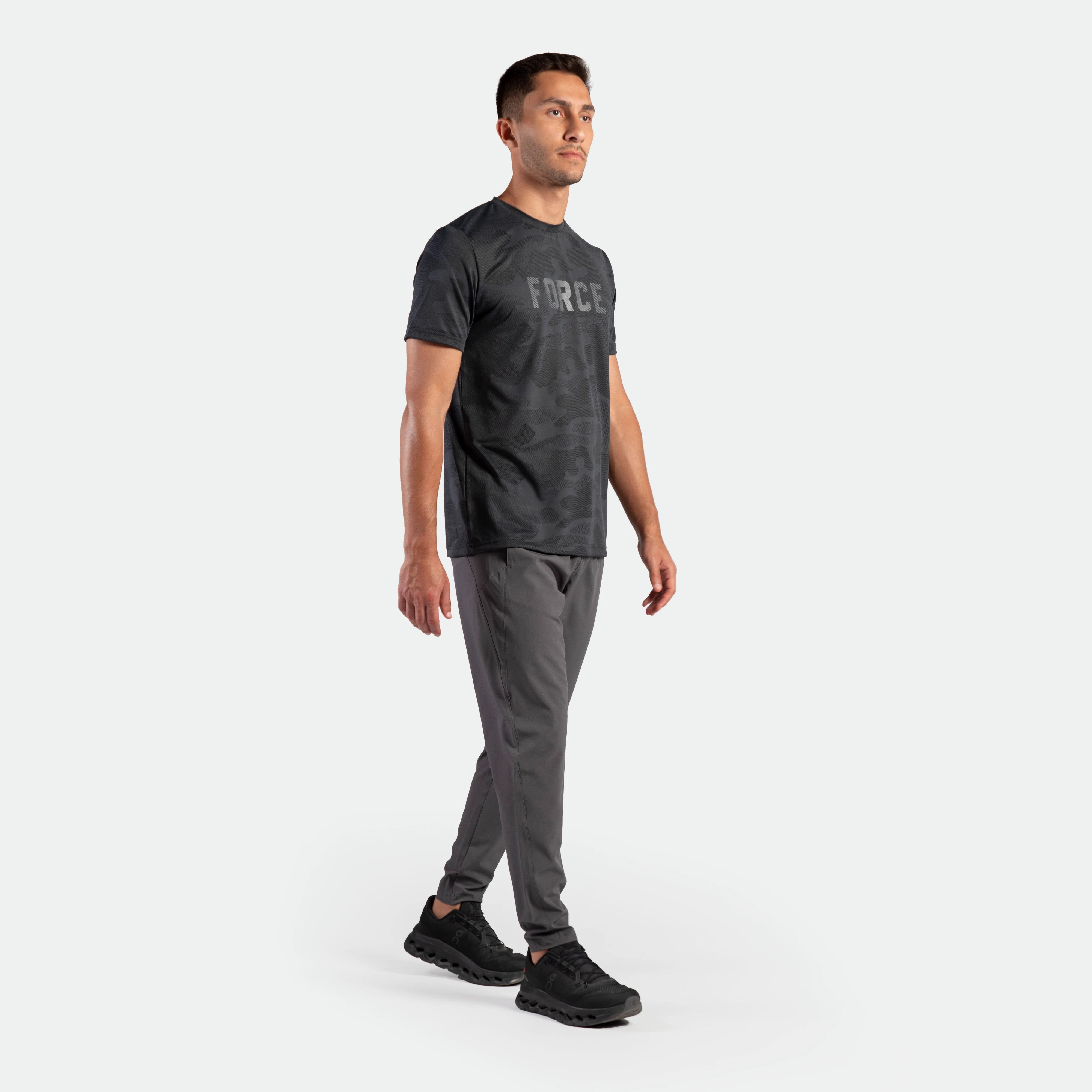 a fit man stand at right and wearing t-shirt graphite blue with pants grey ,plus the shoes black 