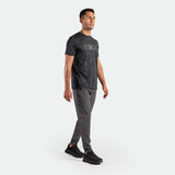 a fit man stand at right and wearing t-shirt graphite blue with pants grey ,plus the shoes black 
