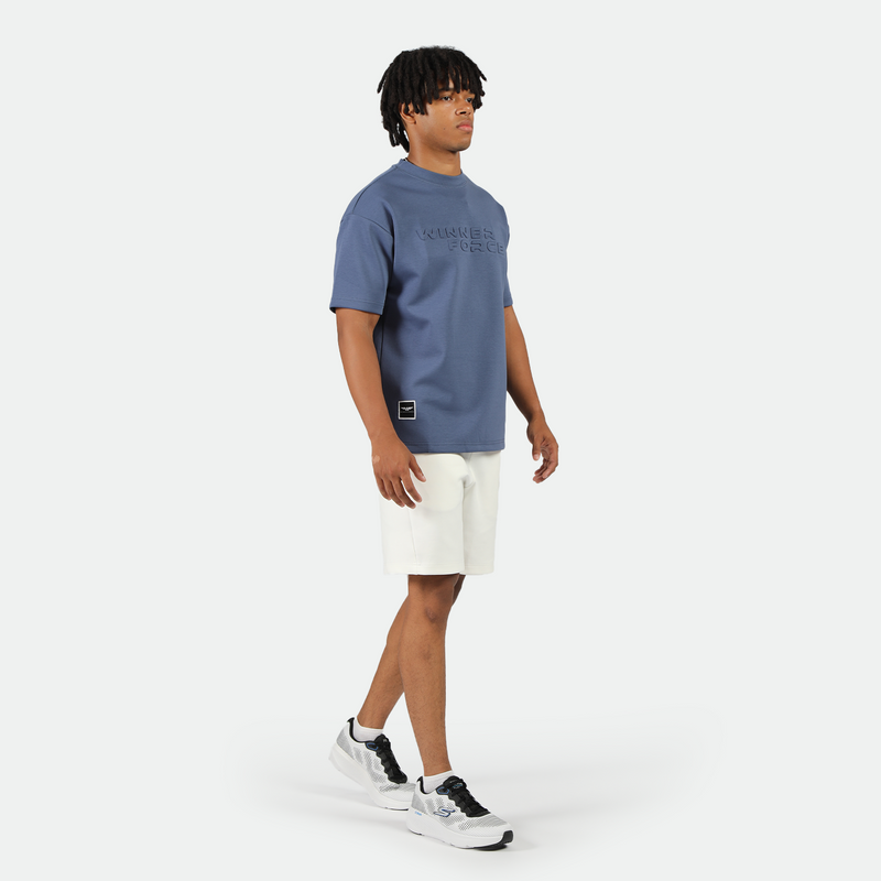 a fit man stand at right and wearing t-shirt indigo blue with short white ,plus short  white with shoes 