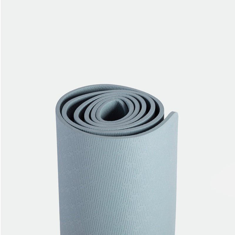 A neatly rolled, light blue yoga mat with a textured surface, set against a plain white background. The image conveys a sense of calm and readiness.