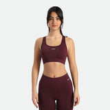 A woman in a dark red sports bra and matching leggings stands in a three-quarter pose, the bra and legging have same  winneforce logo  white In different directions, background is white