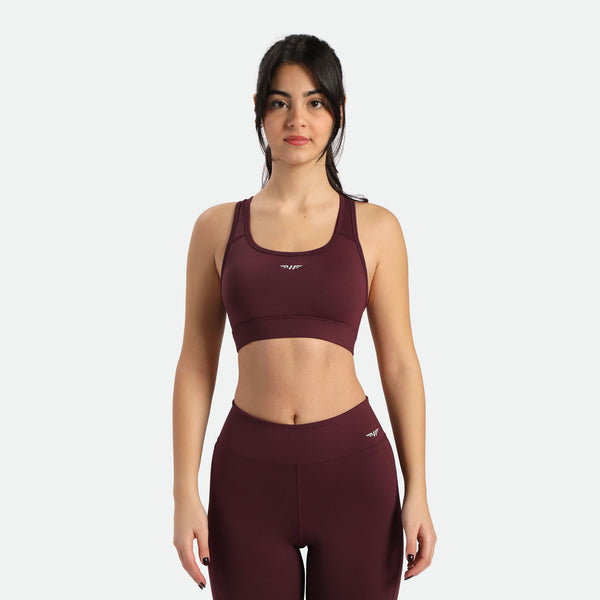 A woman in a dark red sports bra and matching leggings stands in a three-quarter pose, the bra and legging have same  winneforce logo  white In different directions, background is white