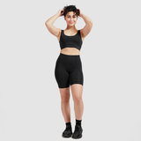 a woman wearing  matching bra and legging ,she stand with  pose,  the hand up  in the hair curly ,she smile plus the background light grey