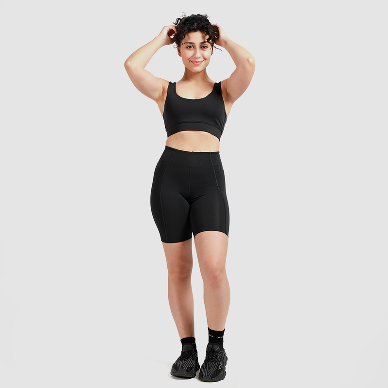 a woman wearing  matching bra and legging ,she stand with  pose,  the hand up  in the hair curly ,she smile plus the background light grey