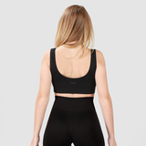 Back view of woman wearing black bra and leggings with background light grey