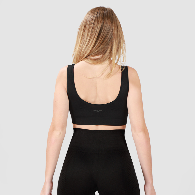 Back view of woman wearing black bra and leggings with background light grey