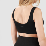 Back view of woman wearing black sports bra and leggings with light gray background