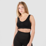 A young woman with shoulder-length blonde hair wearing a black sports bra and high-waisted leggings, posing against a plain light gray background