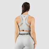A fit woman is seen from the back wearing a light gray athletic outfit, consisting of a sports bra with a strappy back design and high-waisted leggings with "WINNERFORCE" printed on the waistband. Her dark hair is tied back, and she stands against a plain white background