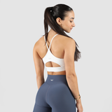 A woman in a stylish white sports bra and blue leggings poses against a plain gray background, showcasing athletic wear.