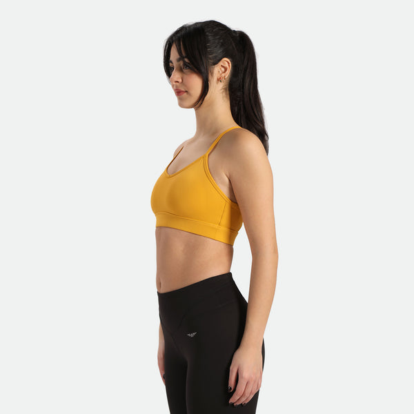 A woman in a yellow sports bra  leggings stands in a three-quarter pose, the bra and legging have the same winneforce logo white In different directions, the background is white