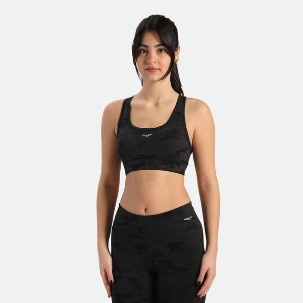 A woman in a camo sports bra and matching leggings stands in a three-quarter pose, the bra and legging have same  winneforce logo  white In different directions, background is white