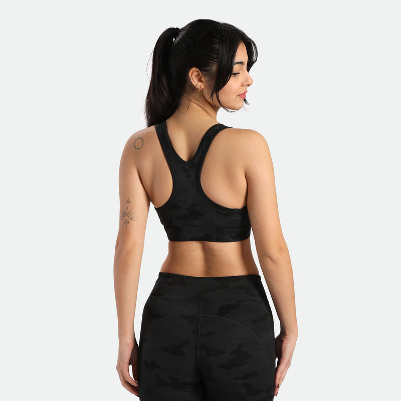 A woman wearing a camo  sports bra and matching leggings stands with her back to the camera