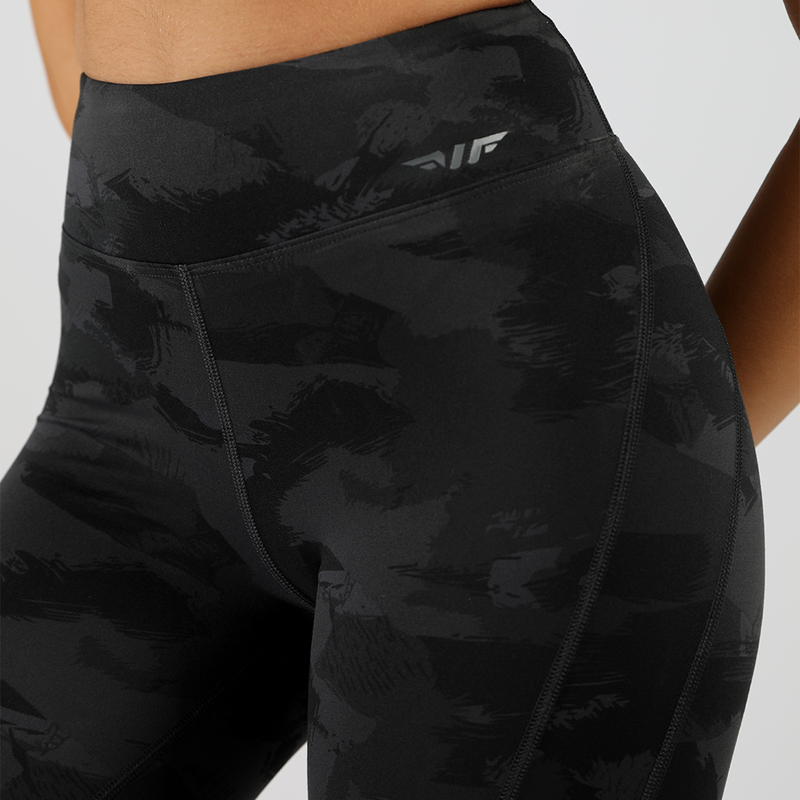 a fit woman wearing camo legging with logo dark grey ,the background is light grey