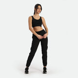 a fit woman stand with pose and look at the camera ,she wearing matching bra and cargo pant with shoes ,plus the background is light grey 
