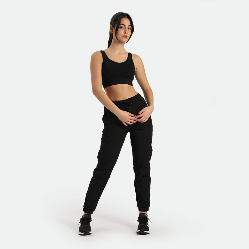 a fit woman stand with pose and look at the camera ,she wearing matching bra and cargo pant with shoes ,plus the background is light grey 