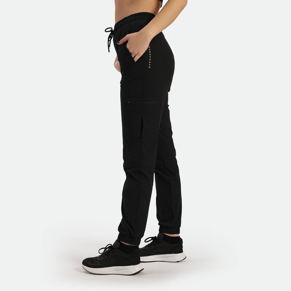 a fit woman stand at right and wearing 
 black cargo pants with shoes ,plus the background is light grey 
