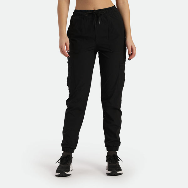 a fit woman wearing cargo black pants with black shoes ,plus the background is light grey 