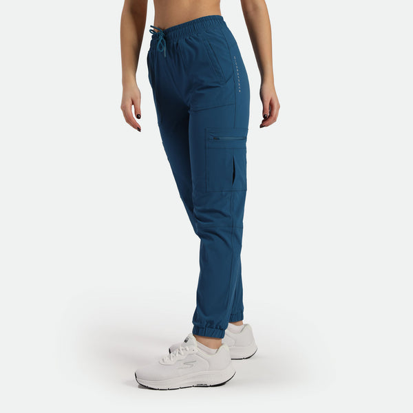 a fit woman stand at right  ,she wearing cargo pant blue with shoes ,plus the background is light grey  