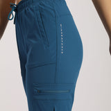  A close-up view of a person wearing blue cargo jogger pants with multiple pockets, including a zippered pocket on the thigh and a vertical printed text design on the side. The pants have an elastic waistband with a drawstring
