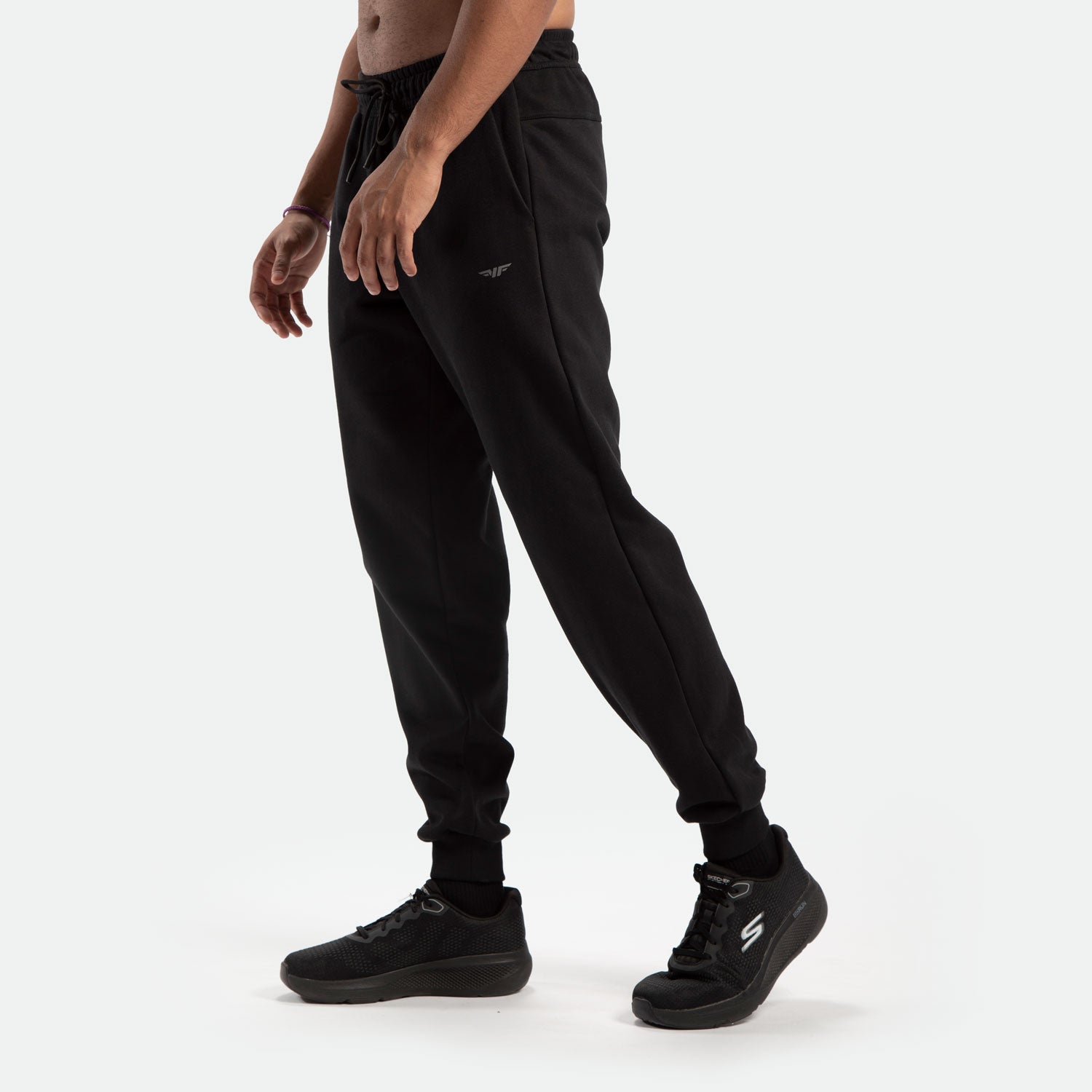 a fit man stand at right and wearing jogger pants black with logo ,plus the shoes black 