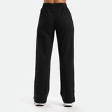 a back view for woman wearing pant  black with black shoes  athletic ,the background is light grey 