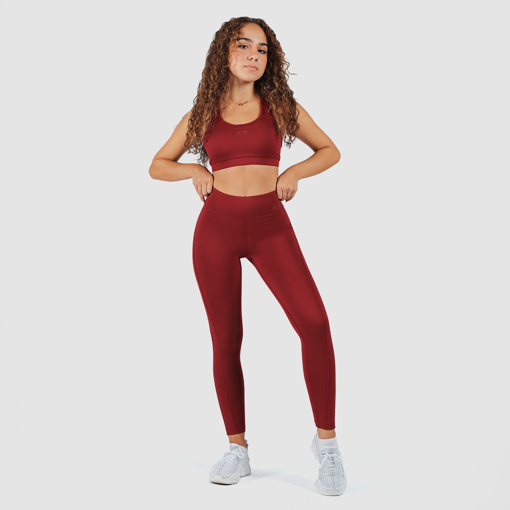 a fit woman look at the camera and stand with pose  ,she wearing matching bra and legging red , shoes white ,plus the background is light grey 