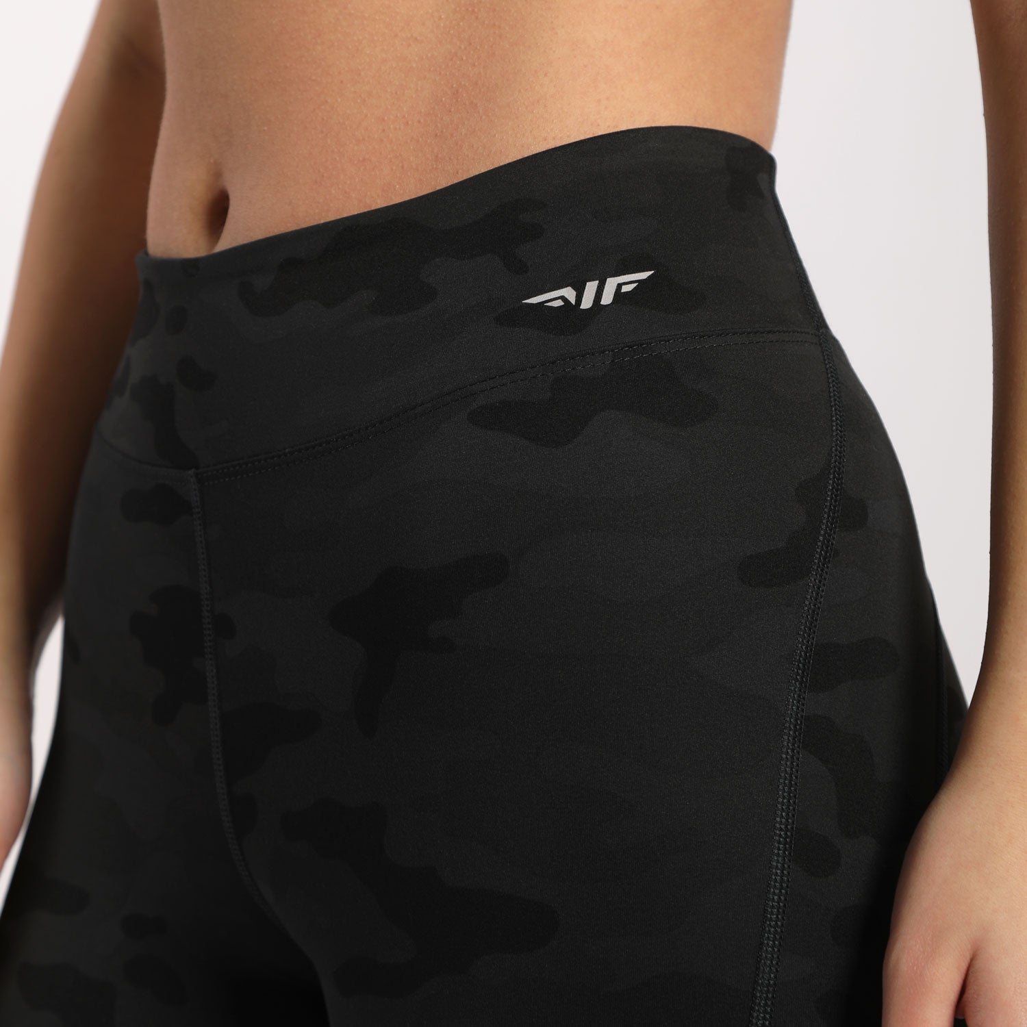 a woman wearing camo legging with  logo white ,plus background  light grey 