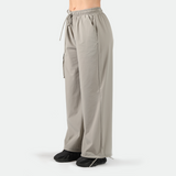 a fit woman stand at right and wearing parachute pants with black shoes athletic ,plus the background is light grey 