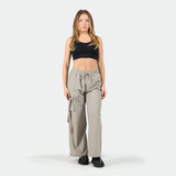a fit woman wearing black bra sports with parachute pants grey and black shoes ,plus  he background is light grey