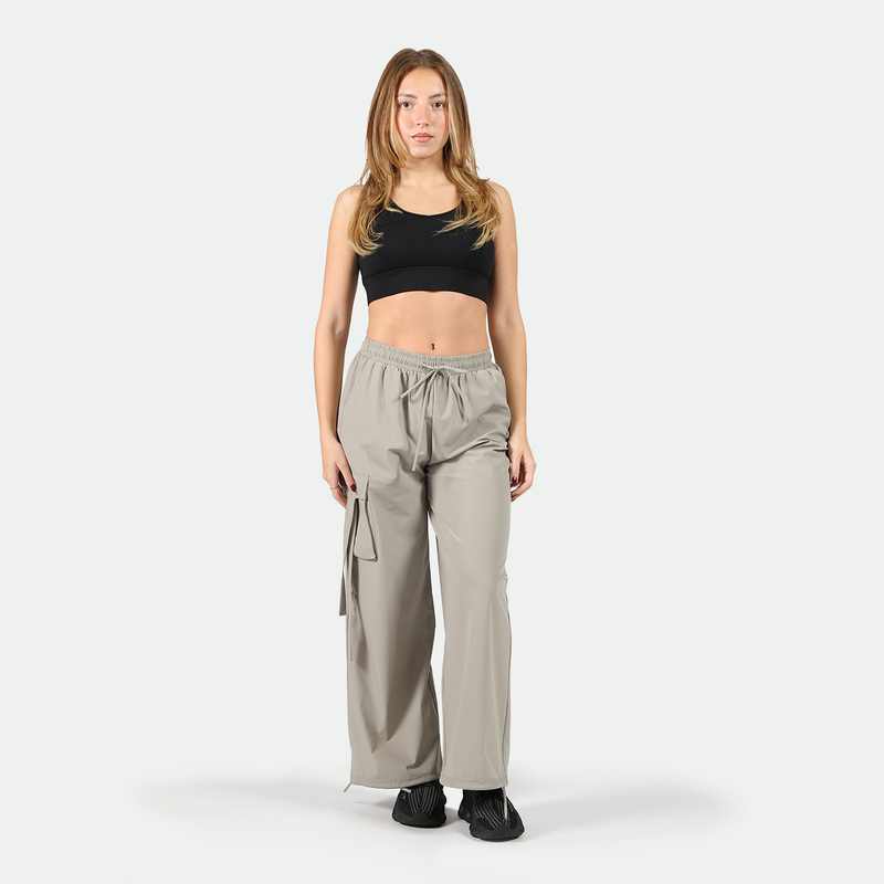 a fit woman wearing black bra sports with parachute pants grey and black shoes ,plus  he background is light grey