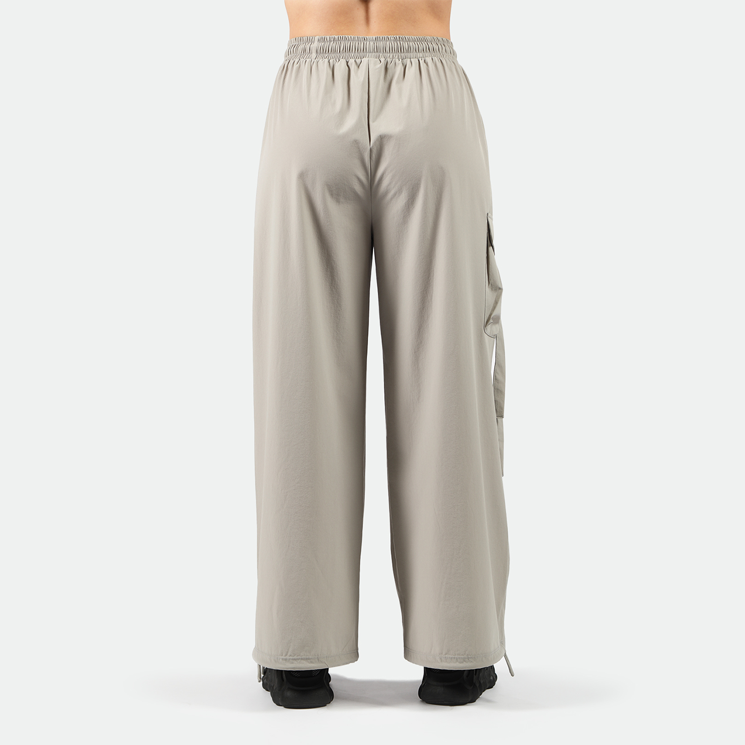 a back view for fit woman wearing wearing parachute pants with black athletic shoes, plus the background is light grey 