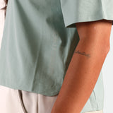 Person wearing a light green shirt with 'Air Force' text, showing an arm with a tattoo.