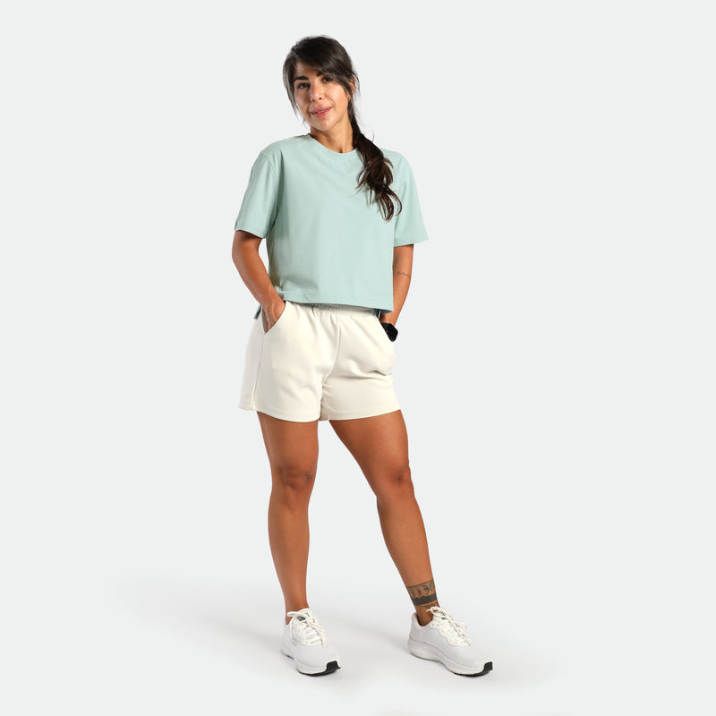 Woman wearing a light green shirt and white shorts on a white background