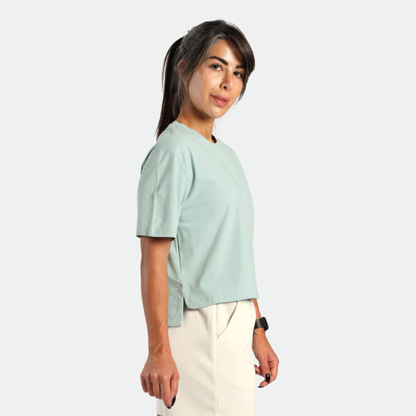 Woman wearing a light green shirt and white pants on a plain background