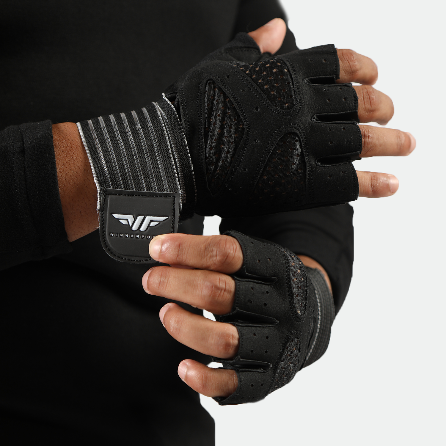 Close-up of hands adjusting black fitness gloves with cut-off fingers and mesh details. The gloves have a logo and striped wrist straps. The tone is focused and athletic.